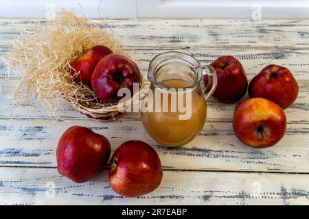 Mele rosse in un cestino e succo di mela in una brocca su un tavolo di legno Foto Stock