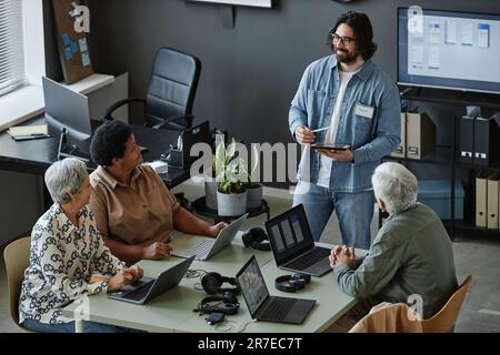 Vista ad angolo alto sul giovane portatore, classe di computer leader per gli anziani che utilizzano i notebook al tavolo Foto Stock