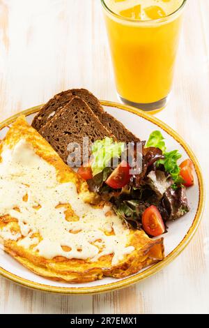 Omelette con formaggio, pomodori, pane tostato e verde su fondo di legno bianco. Concetto di colazione. Foto Stock