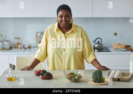 Ritratto di donna afroamericana sorridente alla macchina fotografica mentre prepara il cibo in cucina Foto Stock