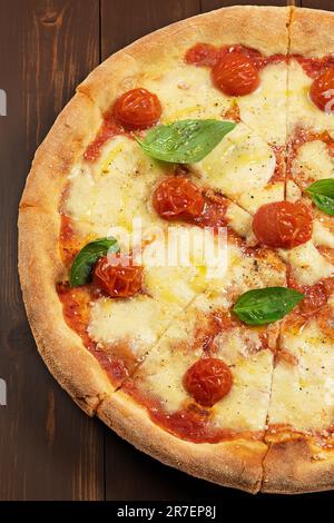 Pizza con salsa di pomodoro, mozzarella fresca, parmigiano e basilico su sfondo ligneo. Foto Stock