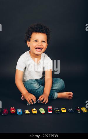 Studio di adorabile bambino africano di 2-3 anni che gioca con mini auto colorate Foto Stock