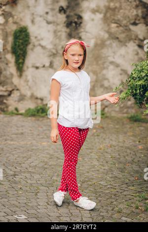 Ritratto di moda all'aperto di una bambina di 8-9 anni che cammina per strada, indossa pantaloni a pois e maglietta bianca Foto Stock