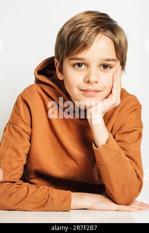 Studio di un bel ragazzo di 10 anni con capelli biondi, con cappuccio marrone, posato su sfondo bianco Foto Stock