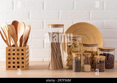 Un set di vasetti di vetro con vari prodotti sfusi e spezie sul piano in legno della cucina. Vano portaoggetti compatto. Stile ecologico in cucina Foto Stock