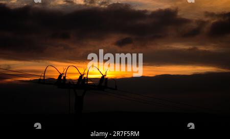 Un bellissimo tramonto illuminato dalla silhouette delle linee elettriche sullo sfondo di colline e nuvole Foto Stock