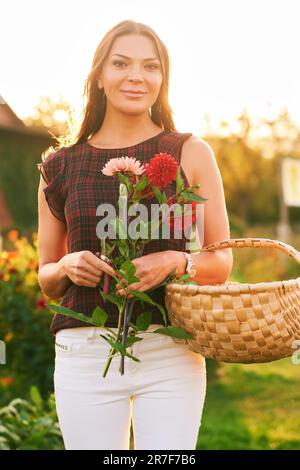 Ritratto all'aperto di bella donna con fiori di dahlia, godendo caldo tramonto in bel giardino Foto Stock