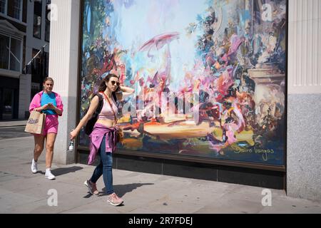 Due donne che indossano sfumature di rosa camminano davanti a una costruzione che ospita un'opera d'arte del raffinato artista, Dairo Vargo, all'angolo di New Bond Street, il 15th giugno 2023, a Londra, Inghilterra. Dairo Vargas, nato in Colombia, è un raffinato artista contemporaneo che trae influenza dal Rinascimento e dal Barocco per creare un legame con il nostro comportamento nella società moderna. Foto Stock