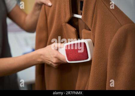 Donna che usa la spazzola per pulire il cappotto di cashmere da polvere e mucchi Foto Stock