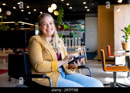 Ritratto di una donna d'affari caucasica in sedia a rotelle che usa un tablet in ufficio Foto Stock