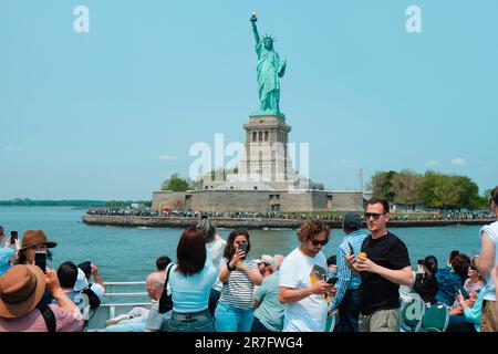 New York City, Stati Uniti - 22 maggio 2023: Un tour in barca pieno di turisti naviga davanti alla Statua della libertà, a Liberty Island, New York, Unit Foto Stock