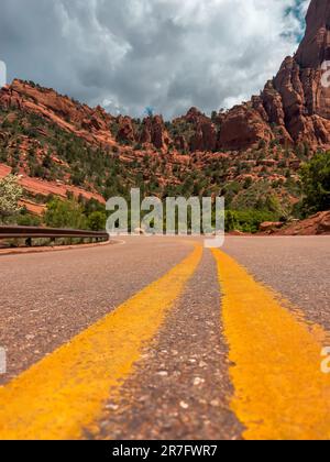 Primo piano di una strada vuota con due linee gialle con splendide montagne rosse sullo sfondo, il parco nazionale di Zion Foto Stock