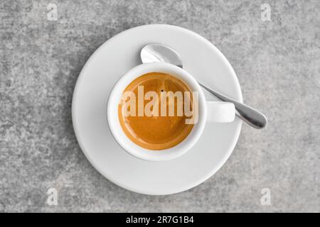 Tazza bianca con fragrante caffè espresso forte e spesse schiume in una caffetteria tradizionale greca. Vista dall'alto del caffè con piattino sul tavolo in marmo grigio Foto Stock