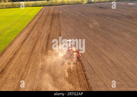 Fotografia in drone di macchine agricole che lavorano in campo coltivato durante la giornata di sole primaverile Foto Stock