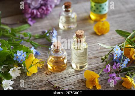 Bottiglie di olio essenziale di aromaterapia con fiori di primavera colorati su un tavolo Foto Stock