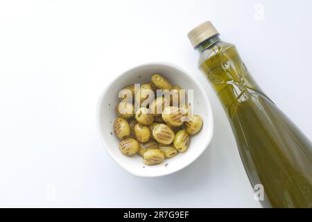 Olive alla griglia turche in una ciotola e bottiglia d'olio su bianco Foto Stock