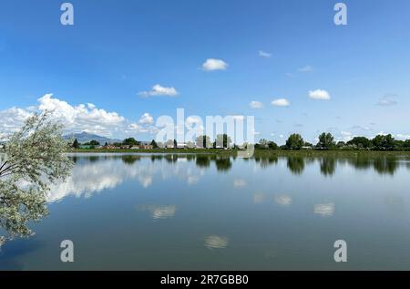 La riflessione sull'orizzonte sul lago Beck a Cody, Wyoming, è vista con il cielo blu, punti nuvolosi bianchi e Heart Mountain sullo sfondo. La terra fa ombre. Foto Stock