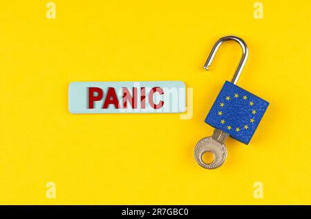 Su una superficie gialla, un lucchetto aperto con l'immagine della bandiera dell'Unione europea con una chiave e un adesivo con la scritta Panic Foto Stock