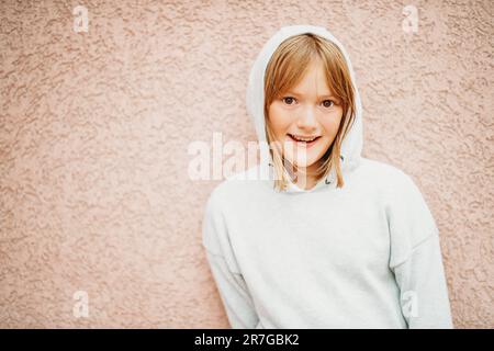 Ritratto all'aperto di divertente bambina che indossa una felpa grigia che si posa su sfondo rosa Foto Stock