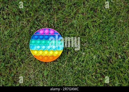 Pop IT Simple Dimple - rotondo silicone sensoriale anti-stress Fidget giocattolo multicolore gioco su erba verde, copia spazio. Attrezzi calmanti, adulti e bambini Foto Stock