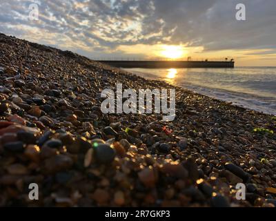 Guardando attraverso una pila decorativa di diverse pietre colorate, ciottoli e ciottoli a Hampton Stone Beach, Hampton Pier in lontananza. Foto Stock