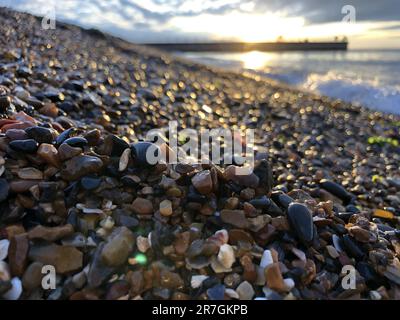 Guardando attraverso una pila decorativa di diverse pietre colorate, ciottoli e ciottoli a Hampton Stone Beach, Hampton Pier in lontananza. Foto Stock