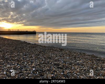 Guardando attraverso una pila decorativa di diverse pietre colorate, ciottoli e ciottoli a Hampton Stone Beach, Hampton Pier in lontananza. Foto Stock