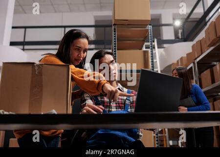 Il commissionatore di magazzino e il responsabile della consegna analizzano la lista di controllo del cliente sul laptop nel magazzino. Magazzino lavoratori asiatici uomo e donna che indicano il programma di logistica del prodotto sul computer Foto Stock