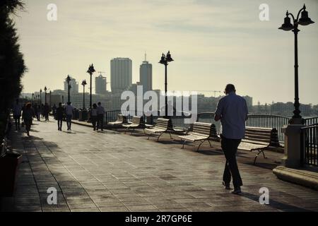 Persone che camminano alla luce del sole dietro sul lungomare di Sliema, sullo sfondo lo skyline di St. Julian's, Malta Foto Stock