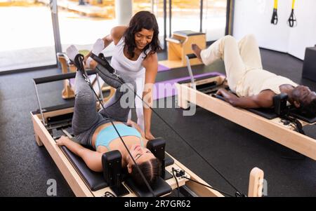 Istruttrice di pilates femminile ispanica che aiuta la giovane donna a fare esercizi sull'apparato riformatore Foto Stock