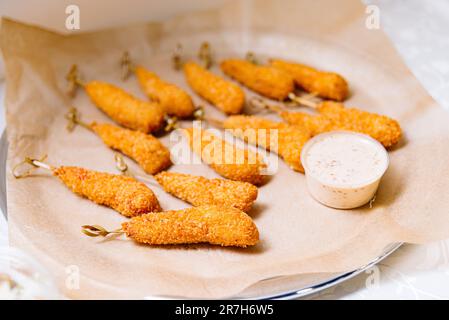 Bocconcini di pollo fritti su spiedini con salsa cremosa su un piatto Foto Stock