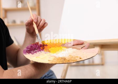 Uomo con pennello e pittura tavolozza artista in studio, primo piano. Utilizzare il cavalletto per sostenere la tela Foto Stock