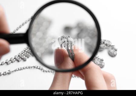 Gioielliere che esamina anello di diamante con lente d'ingrandimento a tavola bianca, primo piano Foto Stock