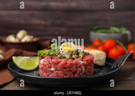 Gustose tartare di bistecca di manzo servite con uova di quaglia e altri accompagnamenti su un tavolo di legno Foto Stock