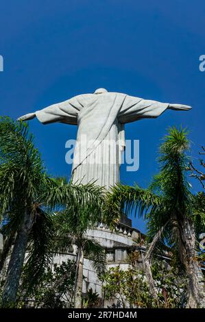 Lato posteriore più vicino della statua del Cristo Redentore vista dalla scalinata del monte Corcovado nel quartiere di Santa Teresa sotto il cielo azzurro e soleggiato d'estate. Foto Stock