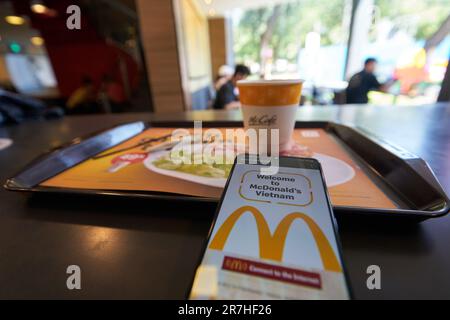 HO chi MINH CITTÀ, VIETNAM - CIRCA MARZO 2023: Il segno Golden Arches visto sul touch screen di smartphone e caffè americano servito sul vassoio a McDona Foto Stock