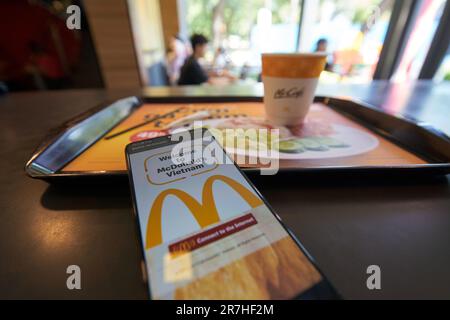 HO chi MINH CITTÀ, VIETNAM - CIRCA MARZO 2023: Il segno Golden Arches visto sul touch screen di smartphone e caffè americano servito sul vassoio a McDona Foto Stock