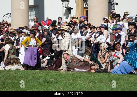 Un gruppo diversificato di persone sorride e si pone per le foto di fronte a un grande raduno di persone, tutti vestiti di abbigliamento festivo Foto Stock