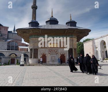 Donne musulmane coperte di colore che camminano di fronte alla fontana del Sultano Ahmed III a destra, Istanbul, Turchia Foto Stock