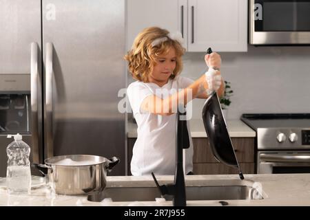 Divertenti ragazzi gemelli che aiutano in cucina con piatti di lavaggio. Bambini che si divertono con i lavori di casa. Bambino che lava i piatti nel lavello della cucina. Foto Stock