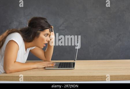 Giovane donna scioccata che non può credere a ciò che vede fissando lo schermo del notebook. Foto Stock