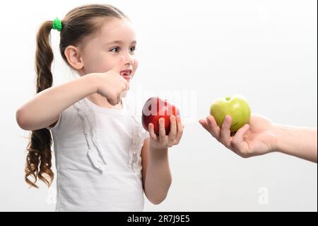 La bambina sceglie fra due mele, mela rossa o verde, scelta del bambino, sfondo bianco e spazio della copia. Foto Stock