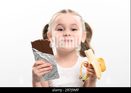 Cioccolato e banana, scelta tra cibo sano e gustoso, sano e ad alto contenuto calorico, bambina sceglie il cioccolato e tenendo banana, copia spazio e Foto Stock