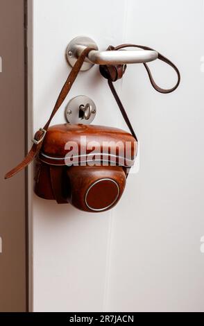 Fotocamera d'epoca appesa alla maniglia della porta su una parete bianca. Foto Stock