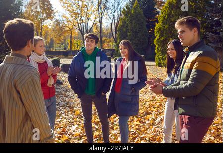 Amici sorridenti e felici di comunicare e godere di camminare attraverso il parco autunnale in una giornata calda e soleggiata. Foto Stock