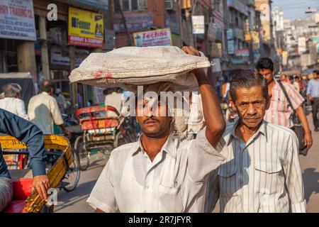 Nuova Delhi, India - 17 novembre 2011: vita di strada al più antico mercato Chandni Chowk nella vecchia Delhi. Persone che trasportano merci in testa al Meena Bazaar di Cha Foto Stock