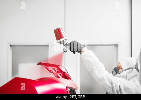 L'operatore dipinge l'auto con la pistola a spruzzo. Paraurti rosso della vettura in una camera di verniciatura durante gli interventi di riparazione. Foto Stock