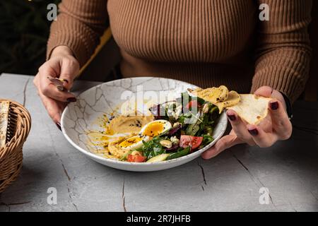 Un hummus femmina che sparge sul pane piatto dalla deliziosa ciotola per la colazione Foto Stock