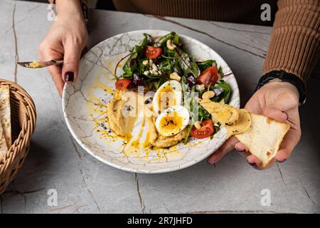 Un hummus femmina che sparge sul pane piatto dalla deliziosa ciotola per la colazione Foto Stock