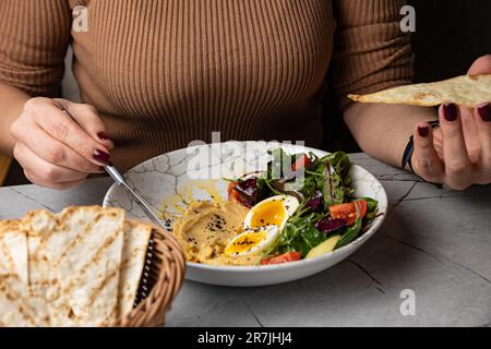 Un hummus femmina che sparge sul pane piatto dalla deliziosa ciotola per la colazione Foto Stock